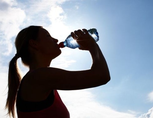 Gegenlichtaufnahme einer Frau, die aus einer Wasserflasche trinkt